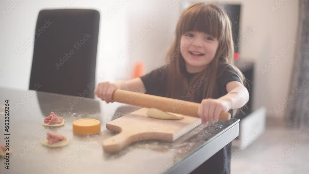 A little girl helps her mother in the kitchen and kneads the dough A little girl helps her mother in the kitchen and kneads the dough