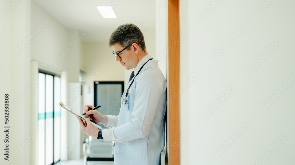 Portrait of Mature Male Doctor Wearing white Coat Standing in Hospital Corridor. Concept Of Medical Technology and Healthcare Business.