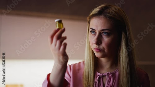 Cruel offended wife looks at bottle with poisonous powder thinking of husband murder during dinner in kitchen close view slow motion photo