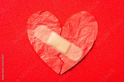 Torn paper heart with adhesive plaster on it. Healing people with broken heart, reunion concept photo