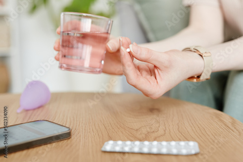 Side view closeup of young woman taking birth control pills with glass of water Fototapet