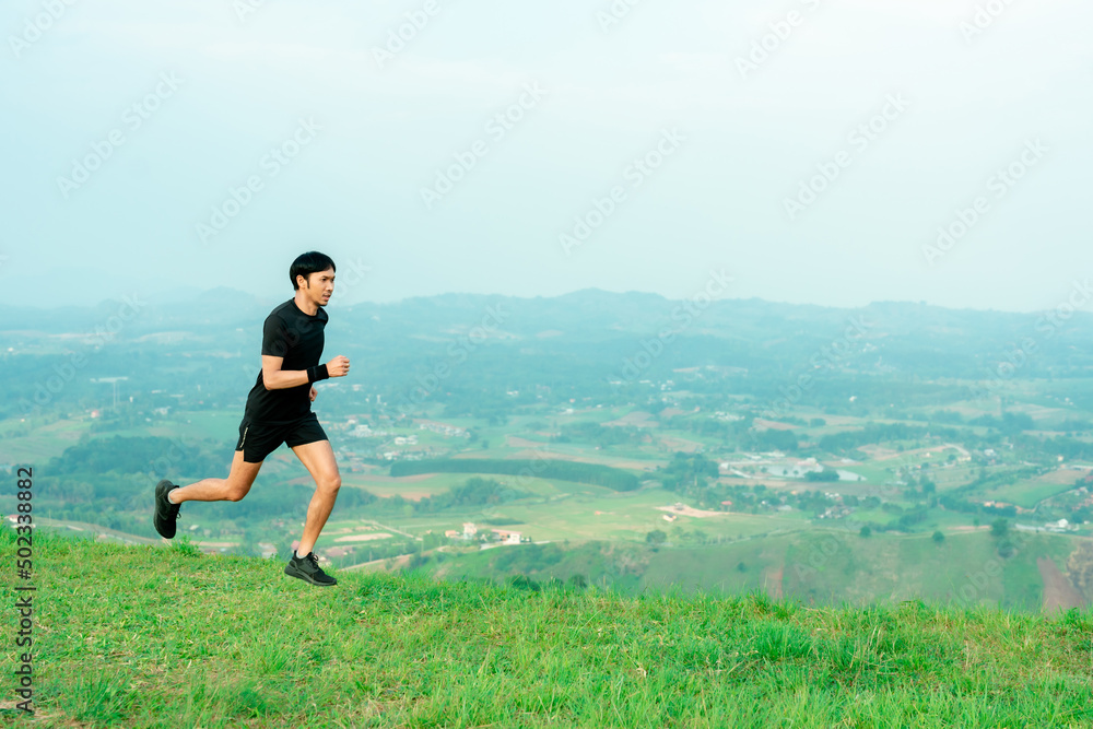 Portrait of an Asian male trail runner running. On the high mountains there are beautiful views. It's a trail running practice. on a bright day Behind is a beautiful mountain view.