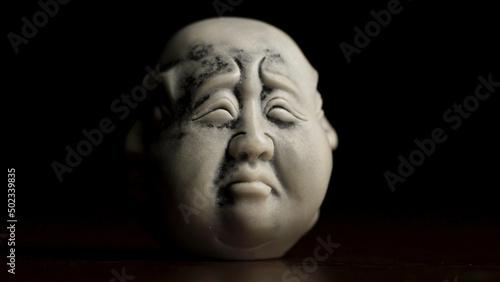 Spiritual enlightenment. Head statue with an emotion sadness. Museum quality statuette against black background. Statuette of a face with an emotion on black background