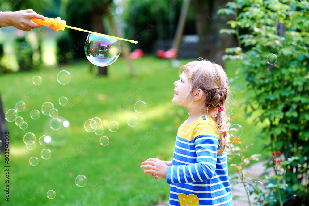 Happy little blonde preschool girl having fun with blowing soap bubble blower. Cute child playing on sunny summer day. Happy active funny healthy kid. Activity for children. Happy little blonde preschool girl having fun with blowing soap bubble blower. Cute child playing on sunny summer day. Happy active funny healthy kid. Activity for children.