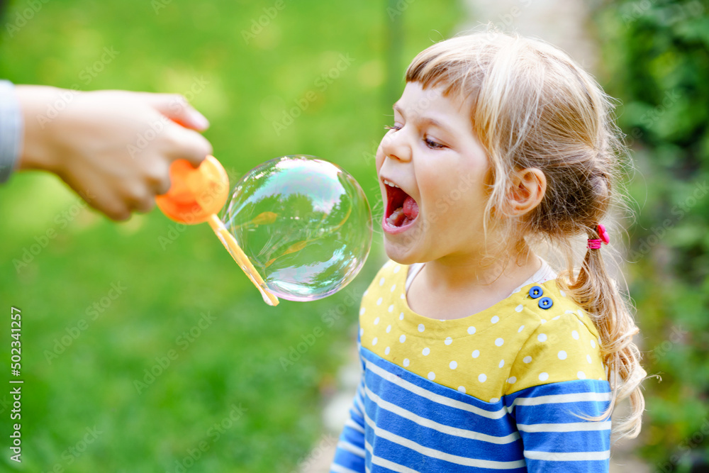 Happy little blonde preschool girl having fun with blowing soap bubble blower. Cute child playing on sunny summer day. Happy active funny healthy kid. Activity for children. Happy little blonde preschool girl having fun with blowing soap bubble blower. Cute child playing on sunny summer day. Happy active funny healthy kid. Activity for children.