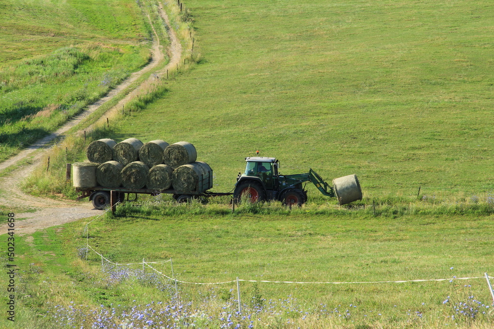Obraz premium Tractor driving hay fresh bale on the field.