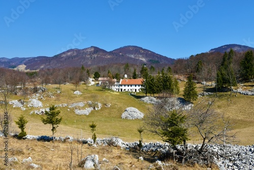 Contryside at the Trnovo forest plateau above Ajdovscina in Slovenia with a farm house and forest covered hills above photo