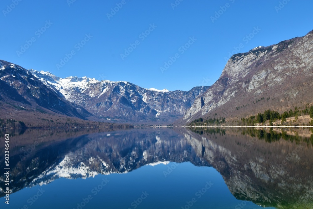 Snow covered mountain peaks in Julian alps and lake Bohinj with the reflection of the mountains in the lake in Gorenjska, Slovenia