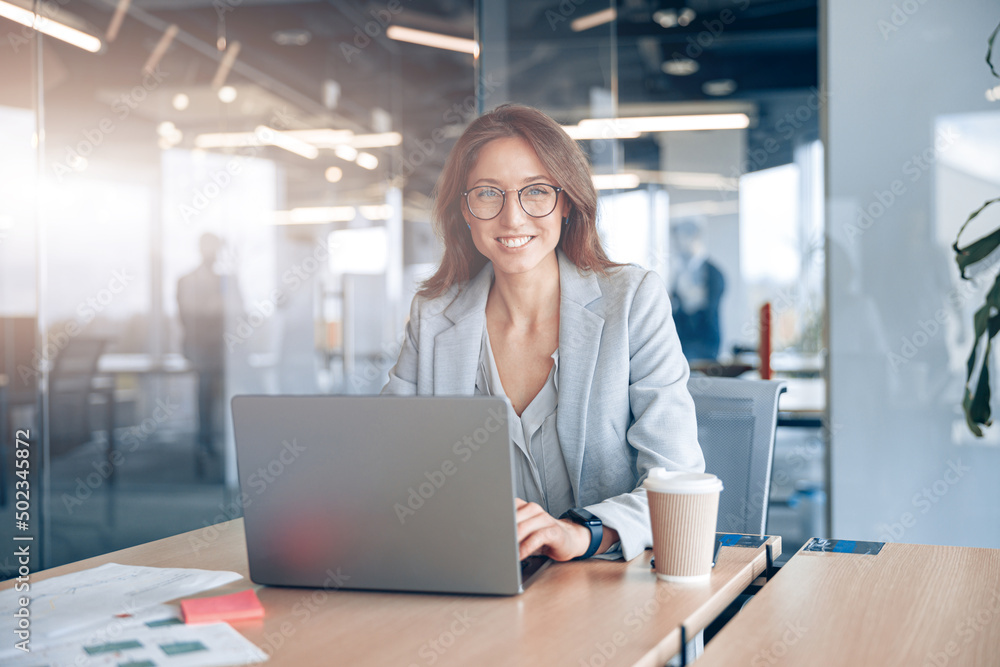 Portrait of smiling businesswoman working on laptop at her workplace at modern office. Portrait of smiling businesswoman working on laptop at her workplace at modern office.