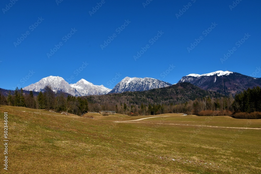 View of snow covered peak of Kocna and Grintovec in Kamnik-Savinja alps and forest covered hills and field in front