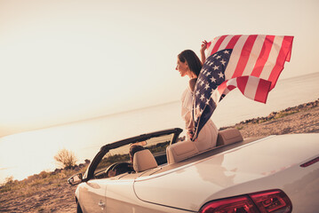 Photo of funny carefree married couple dressed white clothes driving car holding american flag outdoors country side road