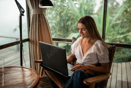 Beautiful young woman using laptop at home, sit near window with nature view photo
