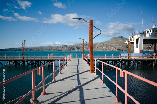 Entrance to jetty, on Lago General Carrera lake, Puerto Ibanez, Aysen, Chile. Pier with street lamps, mooring ropes crosses pier and moored ferry. Pier on glacial lake with mountain view in Patagonia photo
