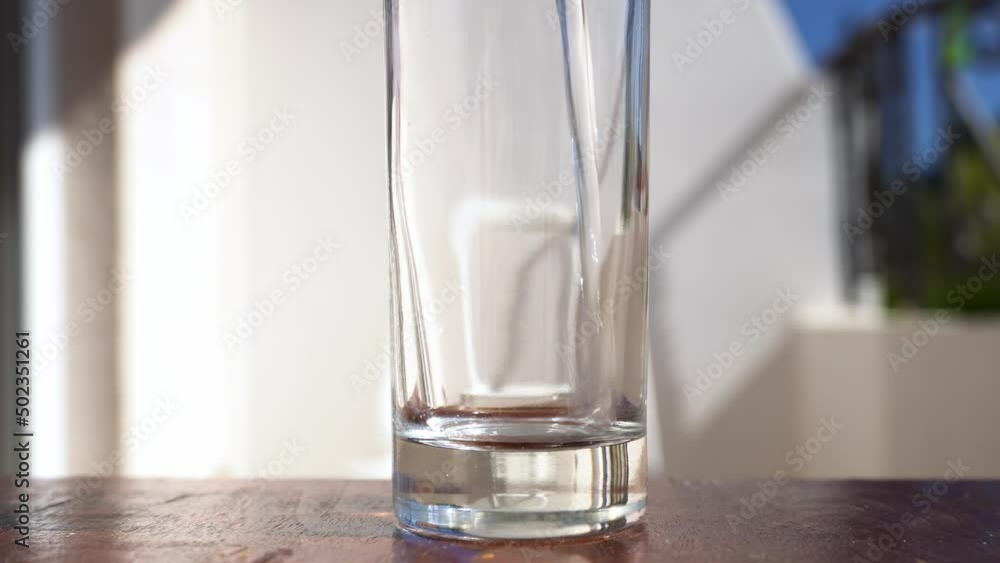 Pouring water into glass from jug at kitchen background. A man pours water into a glass cup on a balcony with a bright sun. Close up Pouring water into glass from jug at kitchen background. A man pours water into a glass cup on a balcony with a bright sun. Close up