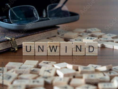 unwind word or concept represented by wooden letter tiles on a wooden table with glasses and a book