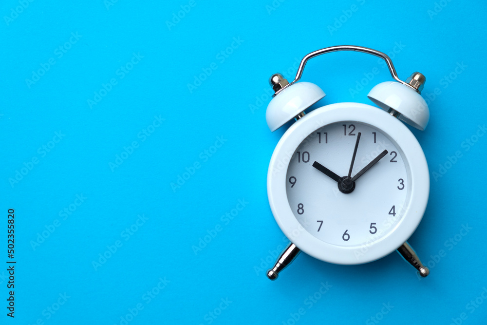 White analog alarm clock isolated on blue background. Concept of time management or business. Copy space. Close-up. White analog alarm clock isolated on blue background. Concept of time management or business. Copy space. Close-up.