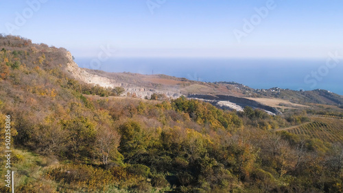 Top view of mining in autumn. Shot. Quarry for mining dug in mountains on background of autumn forest and far sea