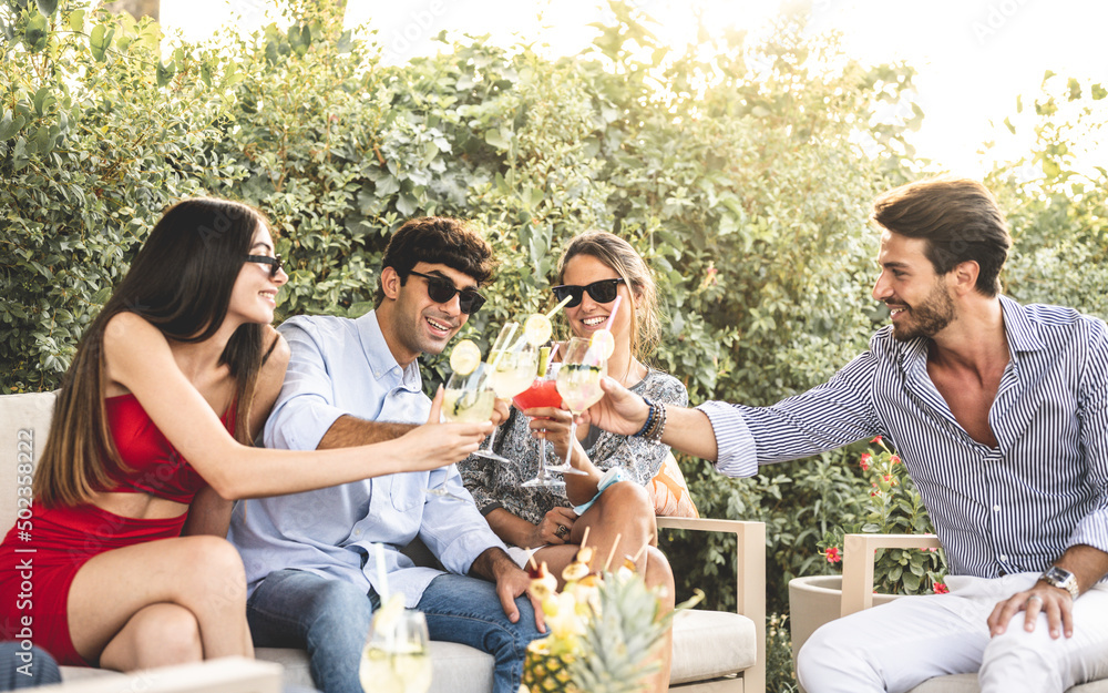 young people at cocktail party, two elegant couples toasting with glasses of fruits coktails, summertime meeting of millennials