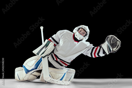 Photography Portrait of teen boy, hockey player, goalkeeper catching plug in motion isolated over black studio background
