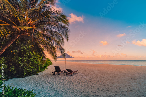 Beautiful tropical sunset scenery, two sun beds, loungers, umbrella palm leaves. Sand, sea view horizon, colorful sunrise sky. Tranquil dusk beach resort. Romantic beach, island paradise landscape