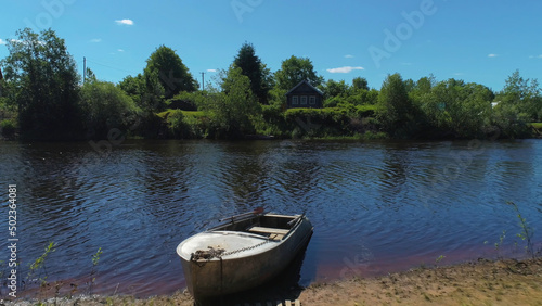 Country landscape with an old wooden house on the lake with a boat. Shot. Bright summer day at the village with green trees and meadow, living in ecological place.