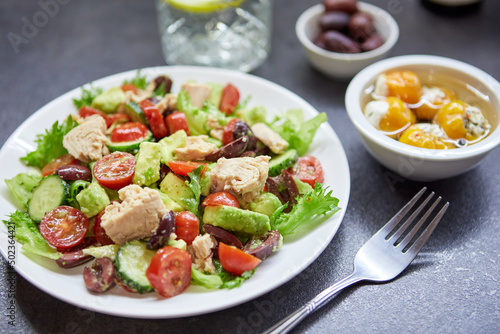 Salad with tuna, lettuce, cucumbers, tomatoes, olives and avocados in white plate on the table