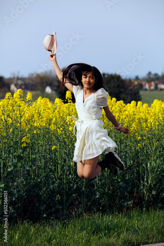 Une jolie jeune fille asiatique saute et salue avec un chapeau devant un champ de colza photo