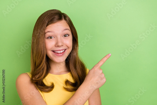 Photo of young cheerful girl indicate finger empty space promotion proposition isolated over green color background