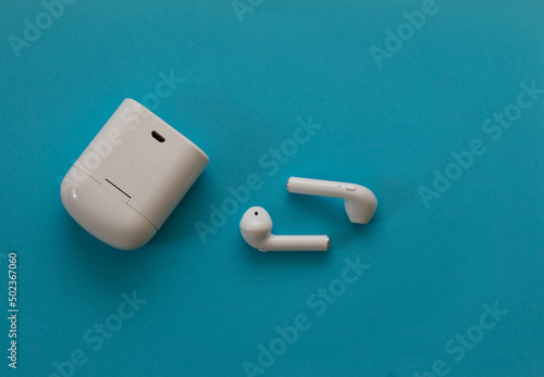 Small white wireless headphones near their holster - against a blue background photo
