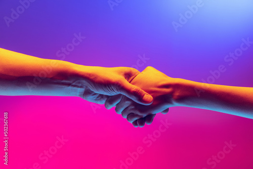 Handshake. Male and female hands touching each other on gradient blue and pink background in neon. Concept of human rights, social issues, gathering.