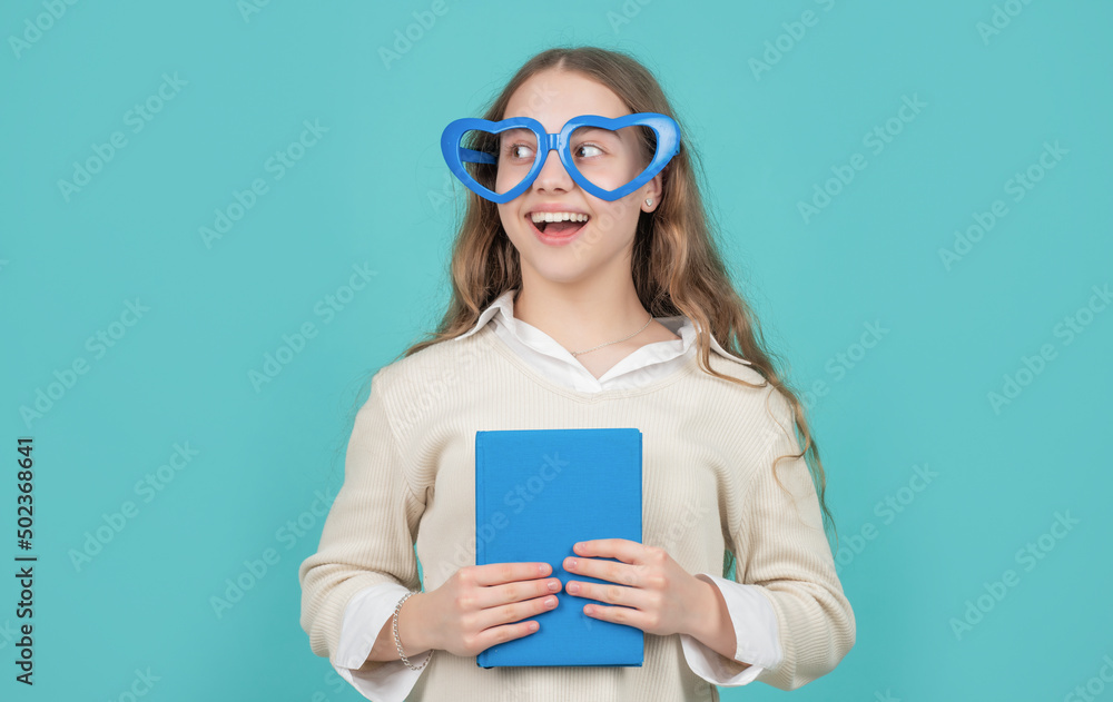 Happy girl back to school with book wearing big funny heart-shaped glasses blue background