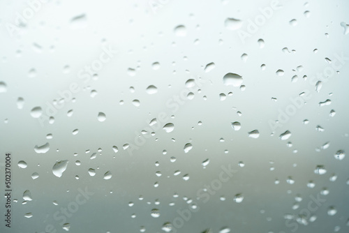 Rain drops on window glasses surface with cloudy background . Natural Pattern of raindrops isolated on cloudy background. Drops of water on glass window over grey background.