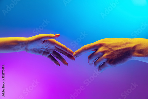Two human hands touch each other isolated on gradient blue-purple background in neon light. Concept of human relation, togetherness, symbolism, culture and history