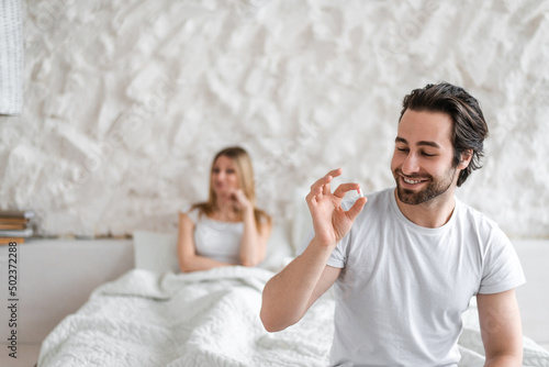 Photos Young man holding pill, solving sexual dysfunction problems, happy woman sitting