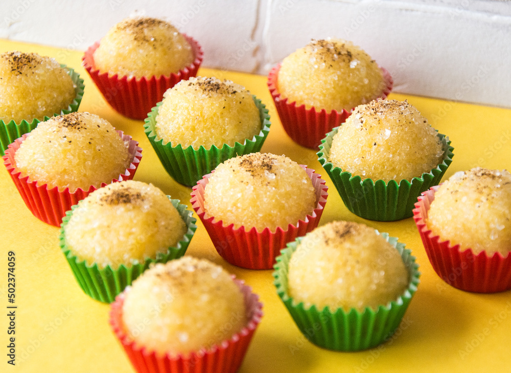 Brigadeiro de milho verde para festa junina em embalagem verde e vermelho na base amarela. Green Corn Brigadeiro for Festa Junina in green and red packaging on a yellow base.
