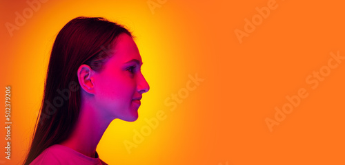 Profile view of young charming girl with long shiny hair isolated on yellow color background in neon filter. Concept of emotions, beauty, fashion, youth.
