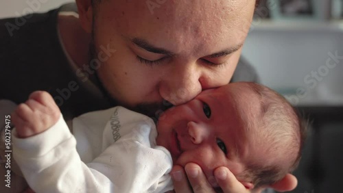 Father hold his newborn baby and kisses him. Enjoying family time.