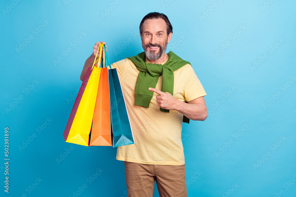 Photo of handsome cheerful person indicate finger store packages isolated on blue color background Photo of handsome cheerful person indicate finger store packages isolated on blue color background