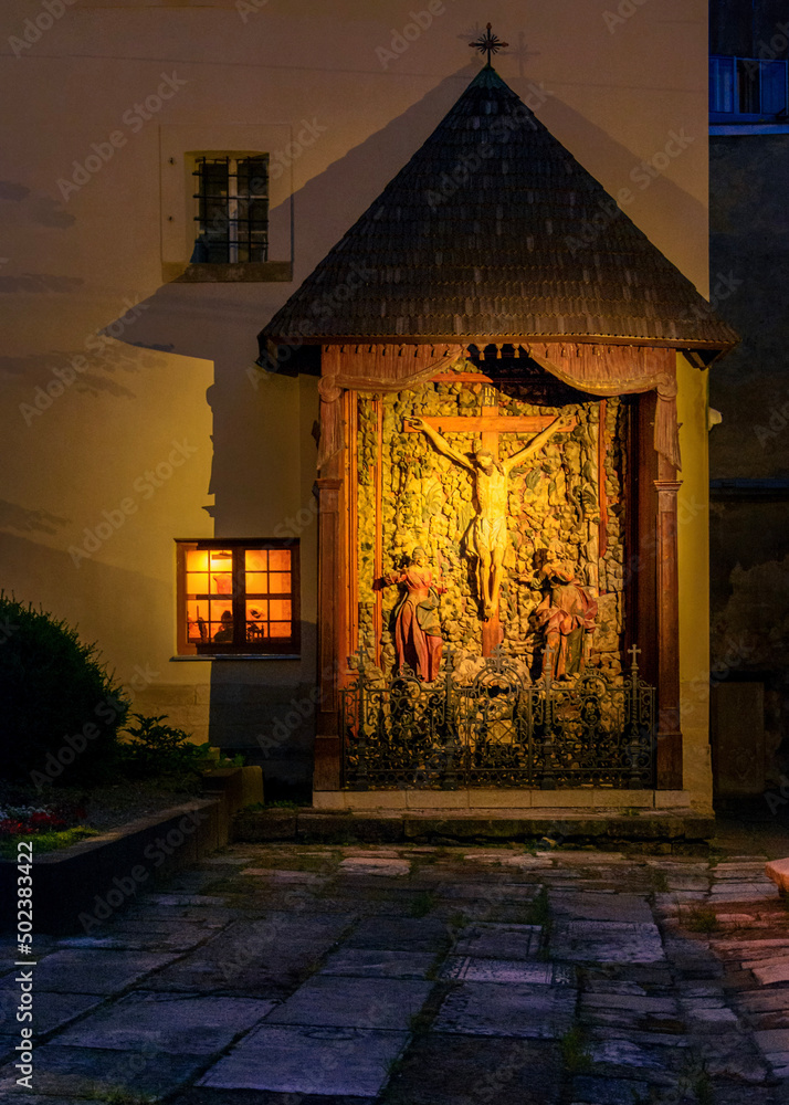 an illuminated window next to a street chapel in Lviv