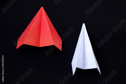 a red paper and white planes on a black background. The concept of leadership, teamwork and courage. © Alena