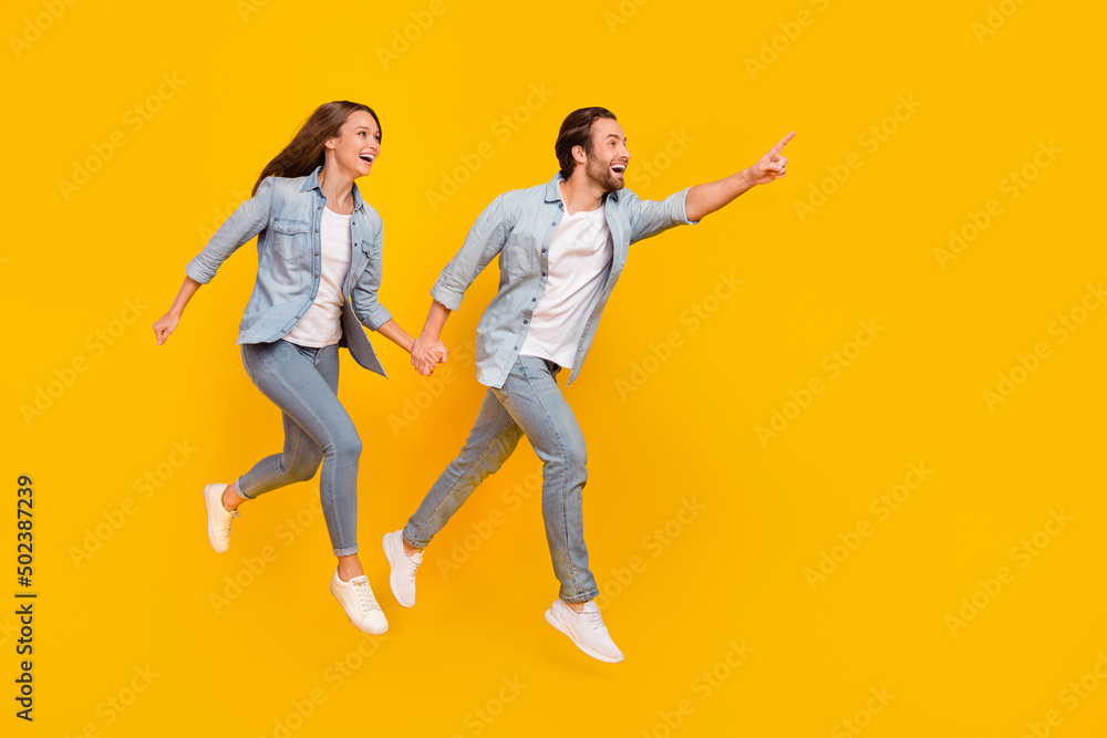 Full length body size view of beautiful handsome couple jumping showing copy space isolated over bright yellow color background Full length body size view of beautiful handsome couple jumping showing copy space isolated over bright yellow color background