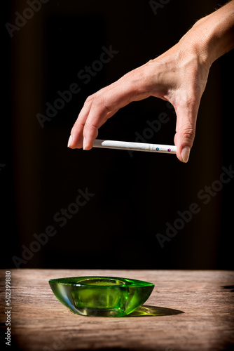 woman's hand holding smoking cigarette with dark background. damage caused by cigarette smoking.