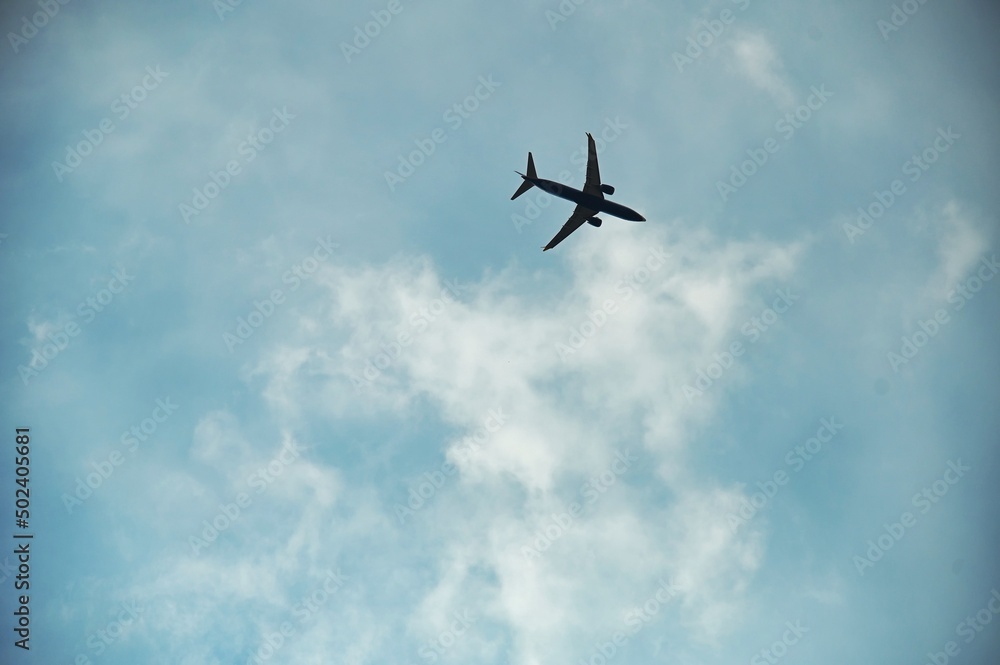 view from below of airplane in flight under blue cloudy sky view from below of airplane in flight under blue cloudy sky