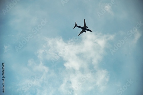 view from below of airplane in flight under blue cloudy sky