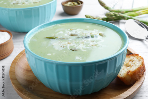 Bowl of delicious asparagus soup served on white wooden table
