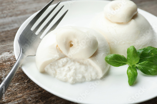 Delicious burrata cheese with basil on wooden table, closeup