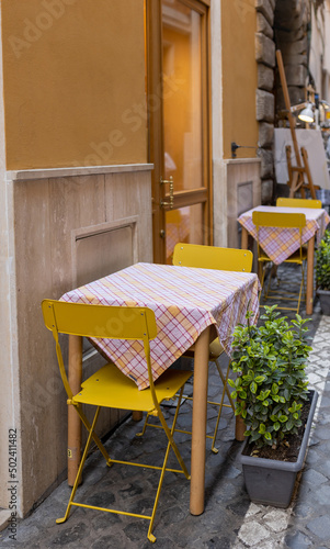 Canvas Print Empty tables and yellow chairs by a trattoria in Rome, Italy