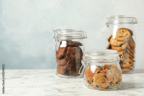 Fotobehang Delicious chocolate chip cookies in glass jars on white marble table, space for