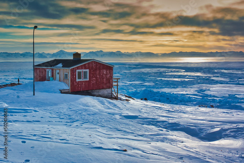 Red lonely wooden house in the sunlight surrounded by snow in Greenland photo