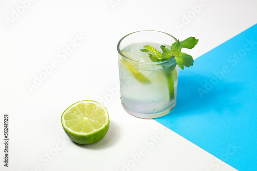 Refreshing detox drink. Water with lime slices and mint leaves. Alcohol drink mojito on abstract white and blue background